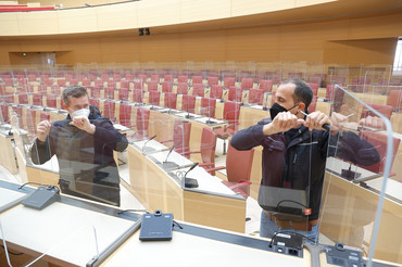 Zwei Männer halten durchsichtige Scheiben im Plenarsaal fest, sie bauen sie ab. 